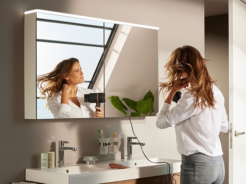 Donna che si asciuga i capelli davanti a uno specchio con luce LED